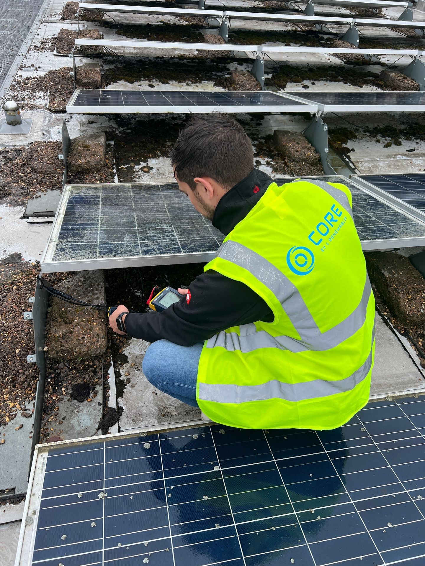 A person in a neon yellow vest checks electrical connections on rooftop solar panels.